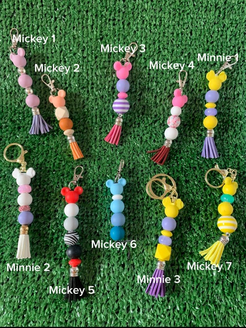 May include: Nine colorful beaded keychains with Mickey Mouse and Minnie Mouse character charms. The keychains feature different colors and patterns, including purple, pink, blue, yellow, and white.