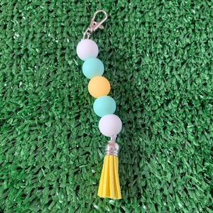 May include: A keychain with a yellow tassel and a string of white, light blue, and yellow beads.