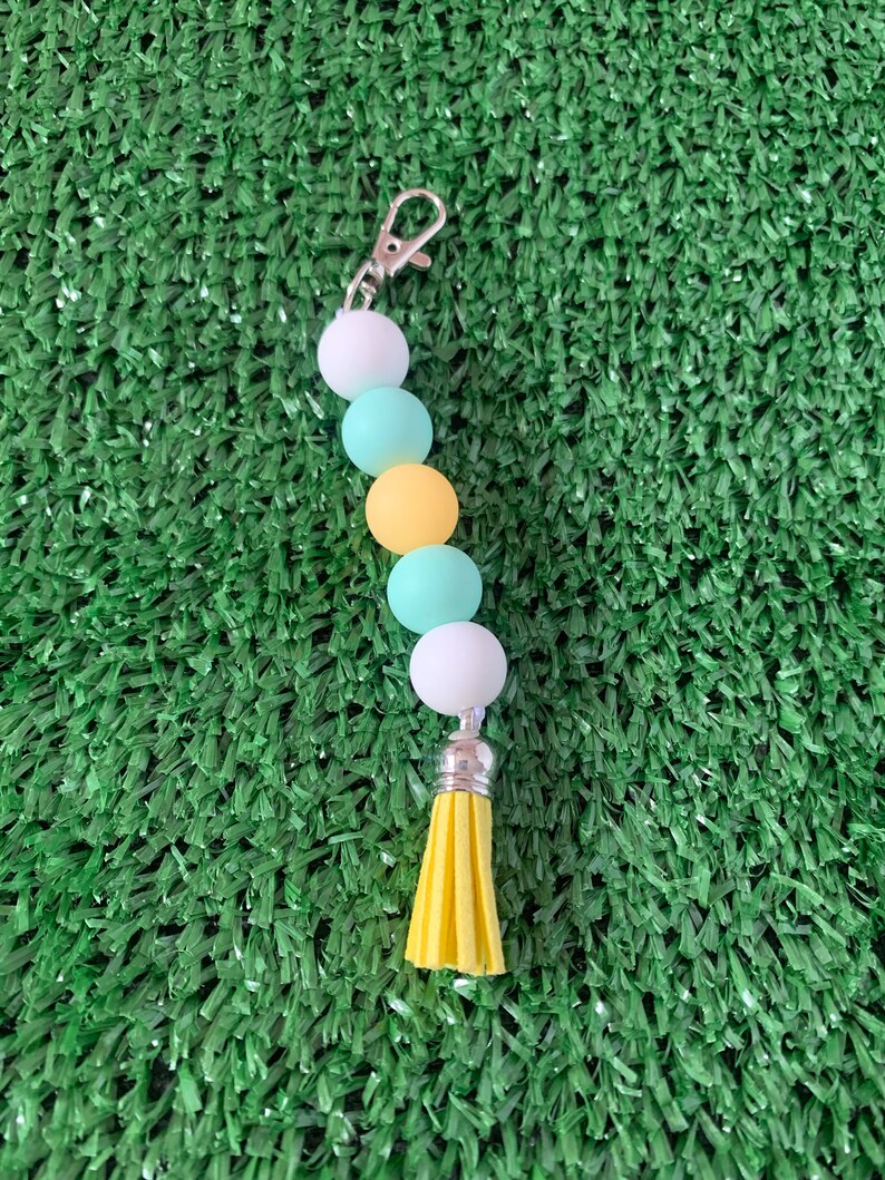 May include: A keychain with a yellow tassel and a string of white, light blue, and yellow beads.