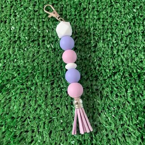 May include: A purple, pink, and white beaded keychain with a tassel. The keychain has a silver clasp.