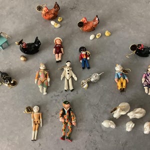May include: A selection of miniature figurines, including chickens, dolls, cats, and clowns. The figurines are painted in various colours and styles, with some featuring gold accents. The arrangement includes a small blue chair and several eggs.