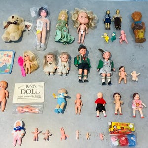 May include: A selection of vintage dolls and toys, featuring a teddy bear, miniature dolls in various outfits, and small plastic figures. The dolls vary in size and style, some packaged and others loose.