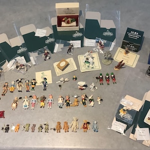 May include: A collection of miniature figurines, including people, animals, and objects, displayed on a light gray surface. Some figurines are in boxes with the "HANTEL" logo. Various colors are present, including brown, blue, and green.