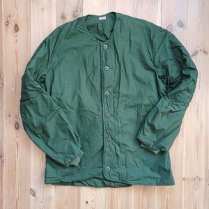May include: A dark green quilted jacket with a button-up front and long sleeves. The jacket has a stand-up collar and a relaxed fit.
