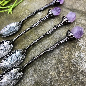May include: Set of four black metal spoons with amethyst crystal handles. The spoons have an ornate design and are perfect for serving desserts or tea.