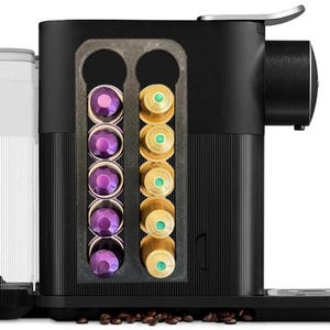Puede incluir: Cafetera negra con un soporte de cápsulas integrado. El soporte tiene varias filas de cápsulas de café, algunas son doradas y otras son moradas.