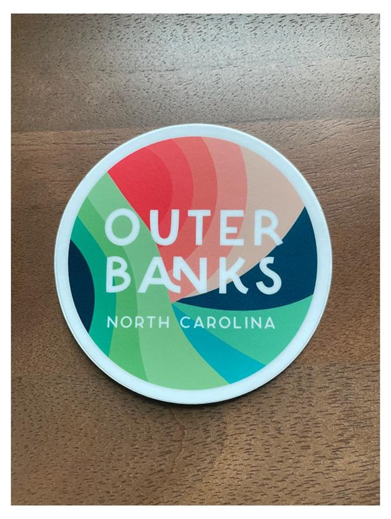 Puede incluir: Una pegatina circular blanca con un dise&ntilde;o abstracto colorido. El texto "Outer Banks" est&aacute; en letras blancas sobre un fondo azul. El texto "North Carolina" est&aacute; en letras blancas sobre un fondo verde.