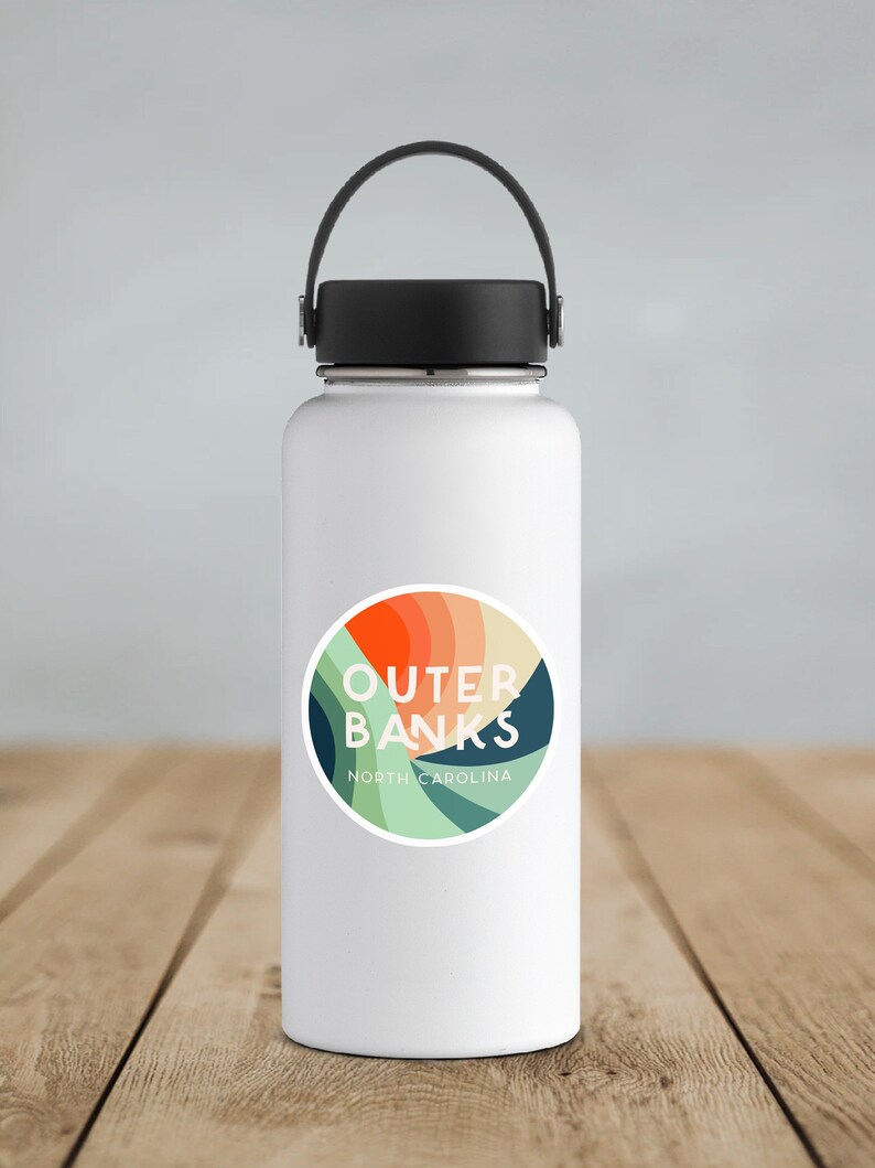 Puede incluir: Botella de agua de acero inoxidable blanca con tapa y asa negras. Una pegatina colorida con el texto "Outer Banks North Carolina" est&aacute; en la botella.