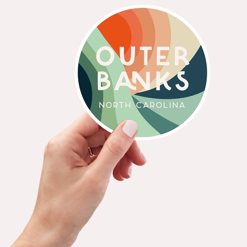 Puede incluir: Una pegatina redonda con un dise&ntilde;o abstracto colorido en tonos naranja, verde y azul. La pegatina dice "OUTER BANKS NORTH CAROLINA" en texto blanco.