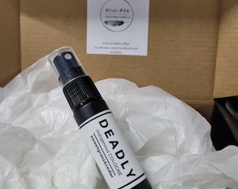 May include: A black cologne spray bottle with a white label that reads "DEADLY Indigenous Cologne sweetgrass&cedar." The bottle is in a cardboard box with white tissue paper. A sticker with text is in the background.