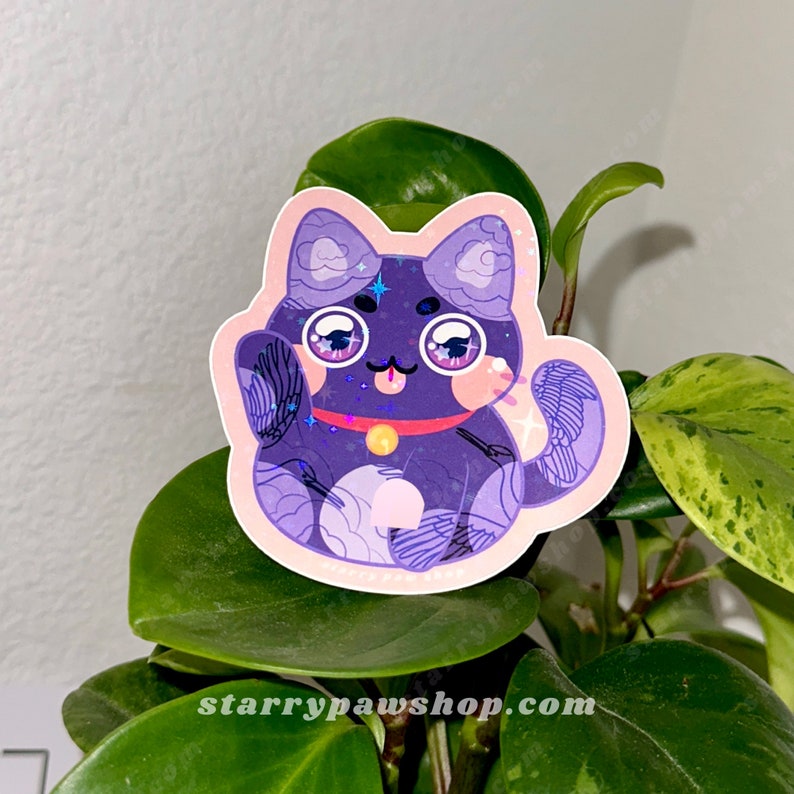 May include: A sticker featuring a purple cat with large eyes, a red collar, and a gold bell. The cat is in a waving pose, with a pink outline. The sticker is placed on a green plant.