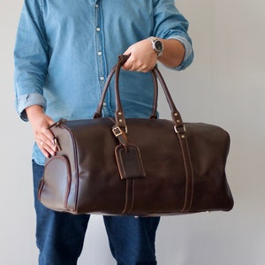 May include: A brown leather duffel bag with a top handle and a shoulder strap. The bag has a luggage tag attached to it.