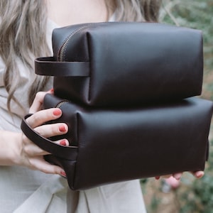 May include: Two brown leather zippered pouches stacked on top of each other. The pouches have a rectangular shape and are made of a soft, supple leather.