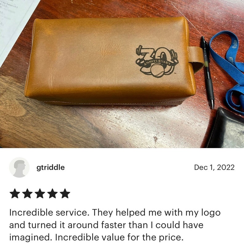May include: A brown leather toiletry bag with a black leather strap and a black logo that says "70th Anniversary".