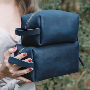 May include: Two stacked blue leather zippered pouches with gold zippers and leather handles.
