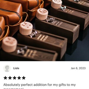 May include: A row of brown leather toiletry bags with personalized wooden boxes containing cufflinks. The boxes are engraved with the names "Chris" and "Cortinas" and the date "03.2022".