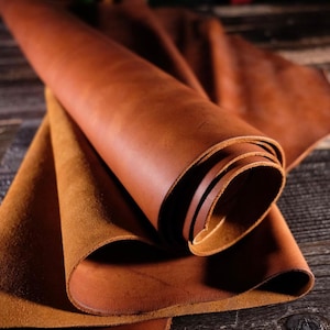 May include: A close-up of a rolled piece of brown leather. The leather is soft and supple, with a natural grain. It is perfect for crafting leather goods.