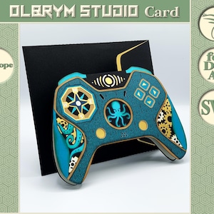 May include: A teal and gold layered paper card in the shape of a video game controller. The controller features a compass rose, an octopus, and gear designs. The card is set against a black background with the text "OLERYM STUDIO Card".