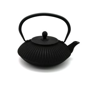Könnte beinhalten: Eine mattschwarze gusseiserne Teekanne mit einem breiten, flachen Körper und einer texturierten, radial gerippten Oberfläche. Sie verfügt über einen passenden runden Deckel mit Knauf und einen festen, bogenförmigen Griff.