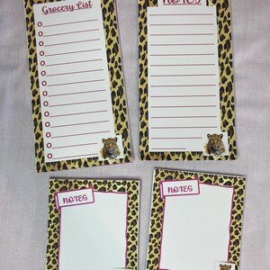 May include: Four notepads with a leopard print border. Two pads are rectangular with lined paper and the words "Grocery List" and "Notes". The other two are square with the word "Notes". Each pad has a small jaguar image.