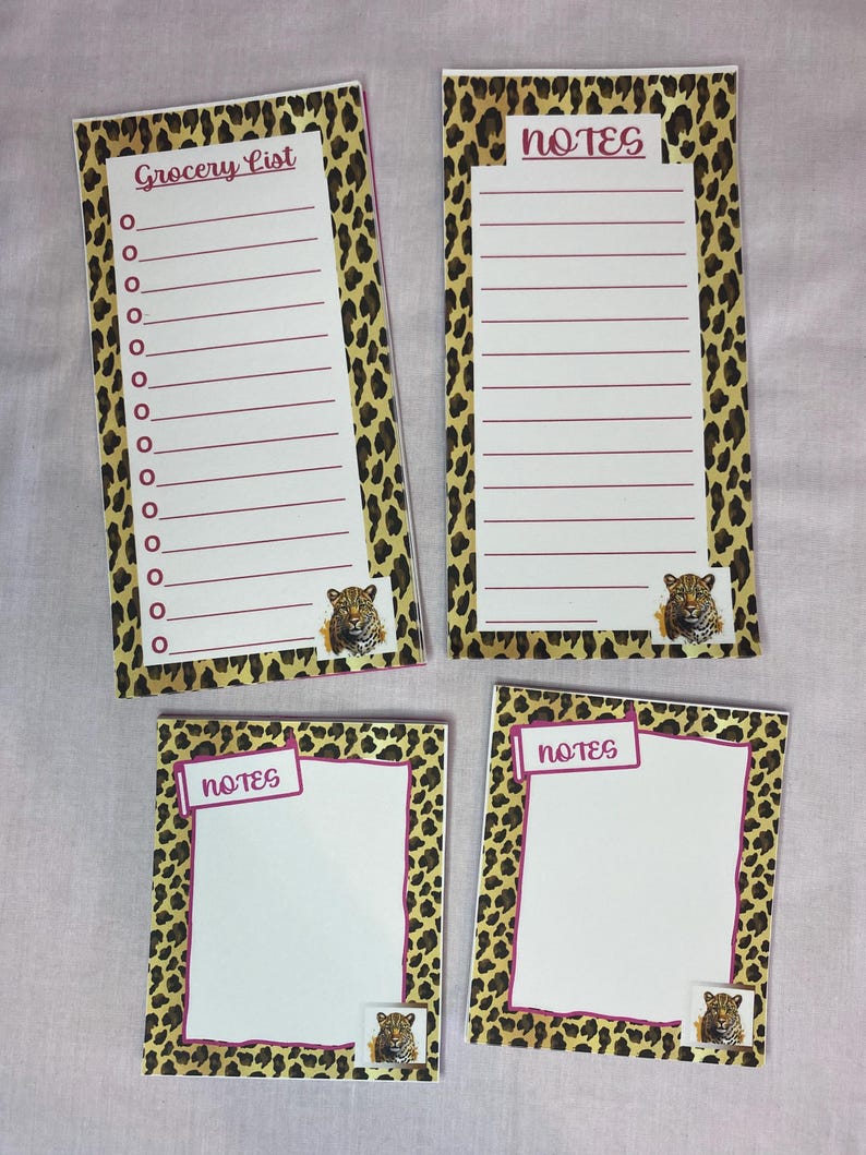 May include: Four notepads with a leopard print border. Two pads are rectangular with lined paper and the words "Grocery List" and "Notes". The other two are square with the word "Notes". Each pad has a small jaguar image.