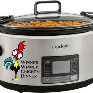 May include: A silver slow cooker with a black handle and lid. The slow cooker has a digital display with buttons for schedule, meal, food, amount, clock, hour, minute, manual, temp, cancel, timer, start, and stop. The slow cooker has a sticker on the front that says "Winner Winner Chicken Dinner" and features a cartoon rooster with big eyes.