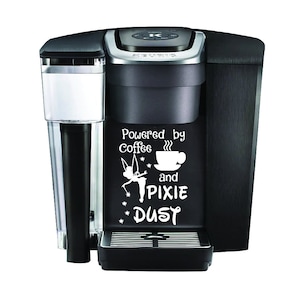 May include: Black Keurig coffee maker with a white decal that says "Powered by Coffee and Pixie Dust" with a fairy and a coffee cup graphic.