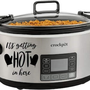 May include: A silver Crock-Pot slow cooker with a black lid and handles. The front of the cooker has a digital display and buttons for setting the time and temperature. The cooker has a black decal that says "It's getting HOT in here" with two oven mitts.