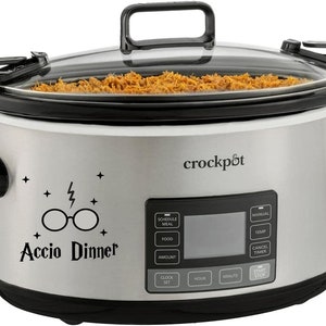 May include: A stainless steel Crock-Pot slow cooker with a glass lid, filled with cooked food. The front features a digital display and the words "Accio Dinner" with a lightning bolt and glasses graphic.