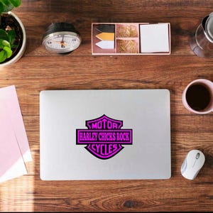 May include: A laptop with a pink and black Harley Davidson logo that reads "MOTOR HARLEY CHICKS ROCK CYCLES". The laptop is on a wooden desk with a coffee cup, mouse, and other office supplies.