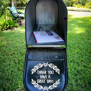 May include: A black mailbox with the words "THANK YOU HAVE A GREAT DAY!" in white script. Inside the mailbox is a white envelope with a red border and a blue and red design. The mailbox is on a wooden post.