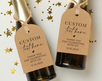 May include: Two small champagne bottles with brown paper gift tags. The tags have black text that says "CUSTOM text here" and "THANK YOU FOR CELEBRATING WITH US! 12.10.2025".