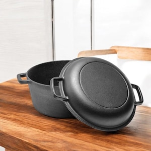 May include: A black cast iron Dutch oven with a lid. The oven is sitting on a wooden surface.