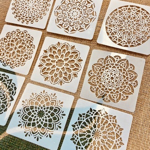 Puede incluir: Conjunto de ocho plantillas de plástico blanco con diseños intrincados de mandalas. Las plantillas son de forma cuadrada y tienen una variedad de patrones.