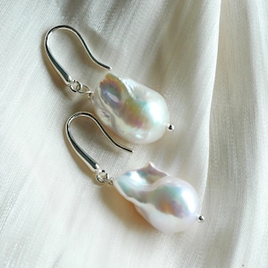 May include: A pair of silver dangle earrings with large, white baroque pearls. The pearls have an iridescent sheen.