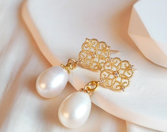 May include: A pair of gold earrings with a delicate filigree design and pearl drops. The earrings are on a white surface.