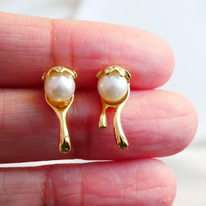 Puede incluir: Pendientes de oro con una perla y un diseño de goteo. Los pendientes son un diseño moderno y elegante.