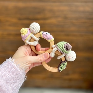 May include: A wooden teething ring with three crocheted animal toys attached. The toys are a watermelon, a green turtle, and a yellow and pink snail.