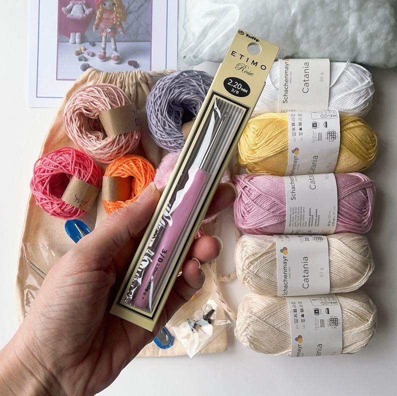 May include: A close-up of a pink crochet hook and a variety of yarn balls in different colors, including pink, yellow, orange, and white. The yarn balls are labeled "Schachenmayr Catania" and are 50 grams each. The crochet hook is labeled "ETIMO Rose 2.20 mm 3/0".