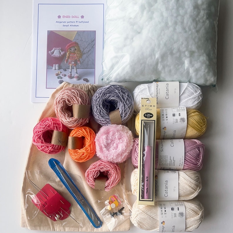 May include: A set of yarn and crochet supplies for making a doll. The set includes a variety of colors of yarn, a crochet hook, stuffing, and a pattern for a doll. The pattern is titled "Enid Doll" and includes the text "Amigurumi pattern heffyland Serpil Altakum".