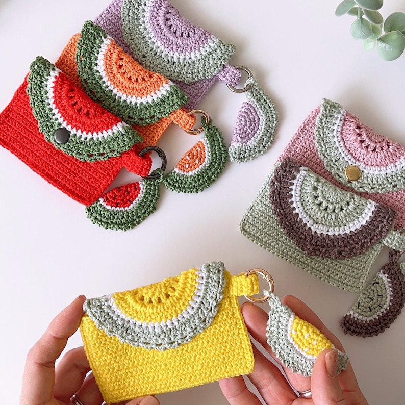 Puede incluir: Cinco monederos de ganchillo con dise&ntilde;os de rodajas de sand&iacute;a. Cada monedero tiene un amuleto de ganchillo a juego. Los monederos son de varios colores, incluyendo rojo, naranja, amarillo, verde, morado y rosa.