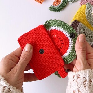 Puede incluir: Una cartera roja de ganchillo con una solapa de ganchillo en forma de sand&iacute;a. La solapa es verde, blanca y roja y tiene un cierre de bot&oacute;n negro.