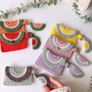 Puede incluir: Cinco monederos de ganchillo con forma de sand&iacute;a con llaveros. Los monederos son de color rojo, amarillo, rosa y morado. Los llaveros tambi&eacute;n est&aacute;n hechos de ganchillo y tienen forma de rodajas de sand&iacute;a.