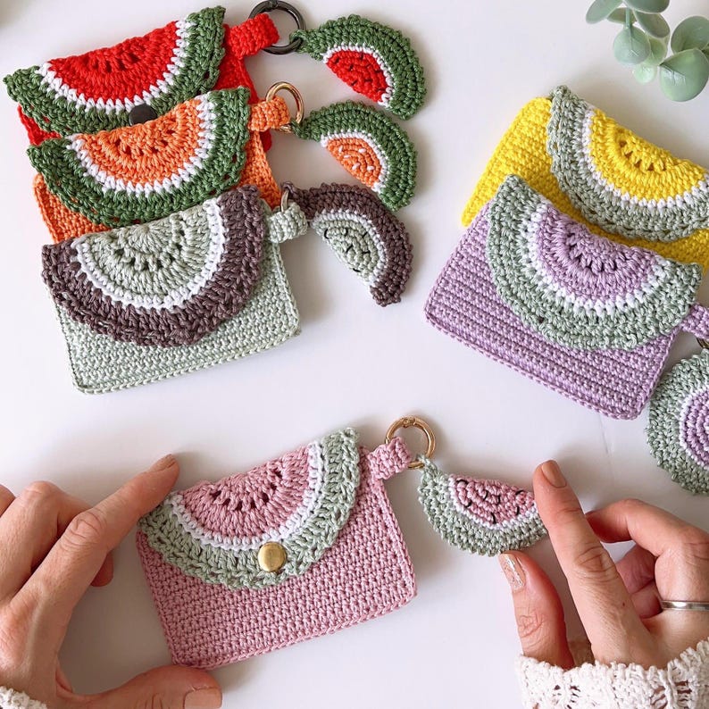 Puede incluir: Cinco monederos de ganchillo con forma de sand&iacute;a con llaveros a juego. Cada monedero tiene un esquema de color diferente, incluyendo rojo, naranja, verde, morado y rosa.