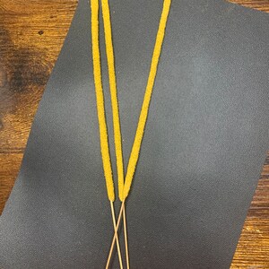 May include: Three yellow incense sticks with wooden bases on a black surface.