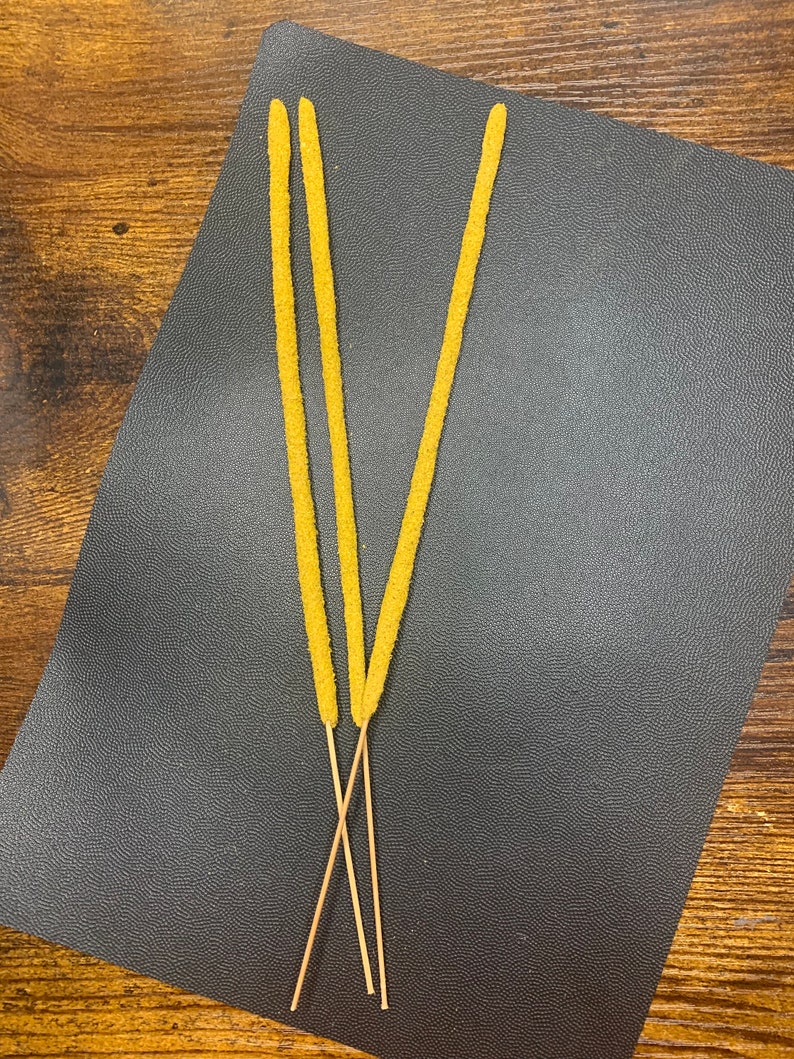May include: Three yellow incense sticks with wooden bases on a black surface.