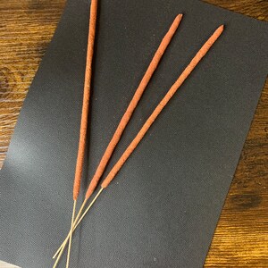 May include: Three brown incense sticks on a black textured surface.