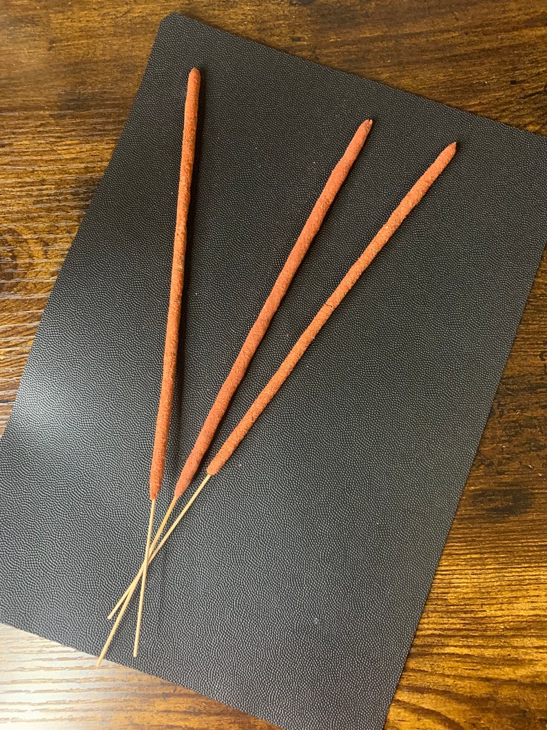 May include: Three brown incense sticks on a black textured surface.