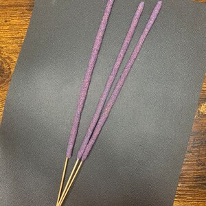May include: Three purple incense sticks with wooden bases on a dark gray surface.