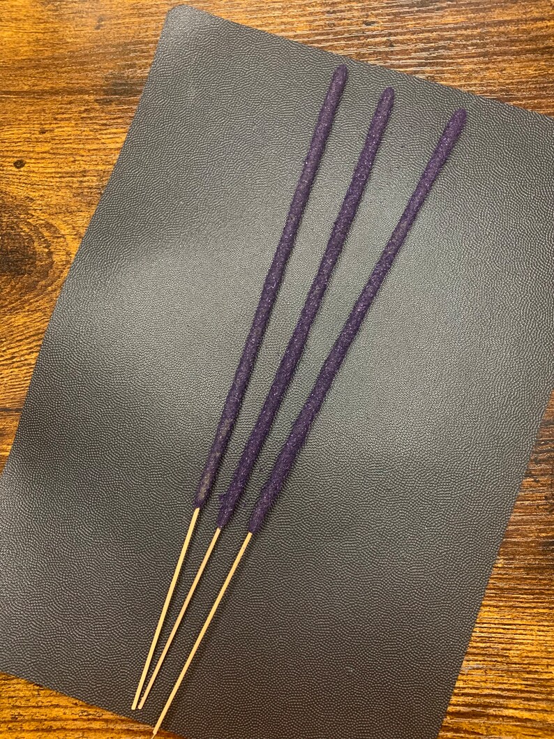 May include: Four purple incense sticks with a gold base on a dark gray surface.